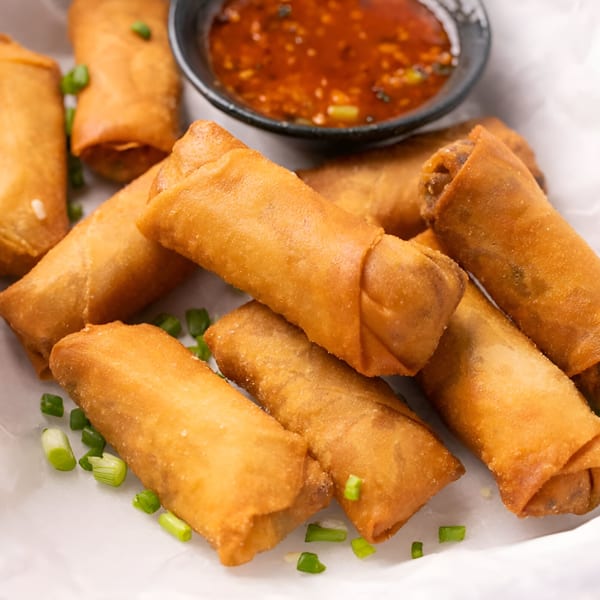 Crispy golden-brown spring rolls with chopped green onions and a side of red dipping sauce.