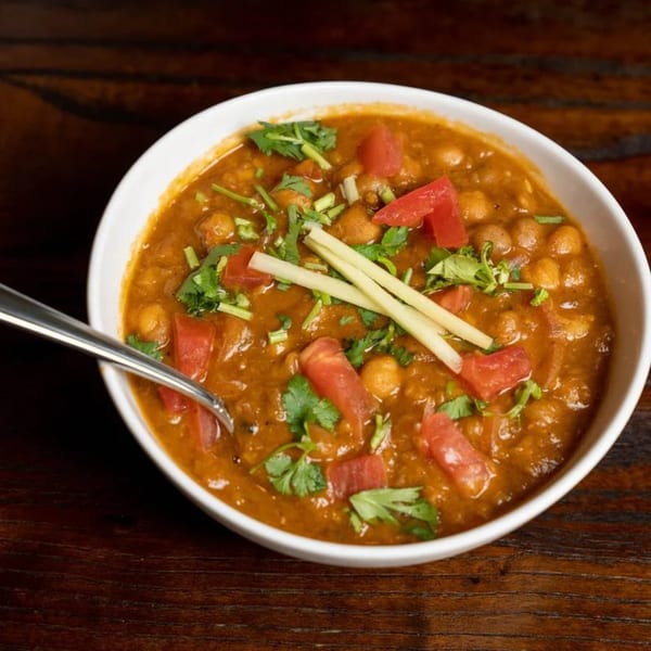 A white bowl of Noorani Kabab House's chana masala, garnished with tomatoes, cilantro, and ginger.