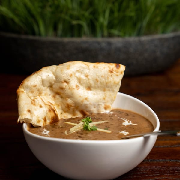 A bowl of Noorani Kabab House's Indian dal makhani, garnished with ginger and cilantro, with naan.