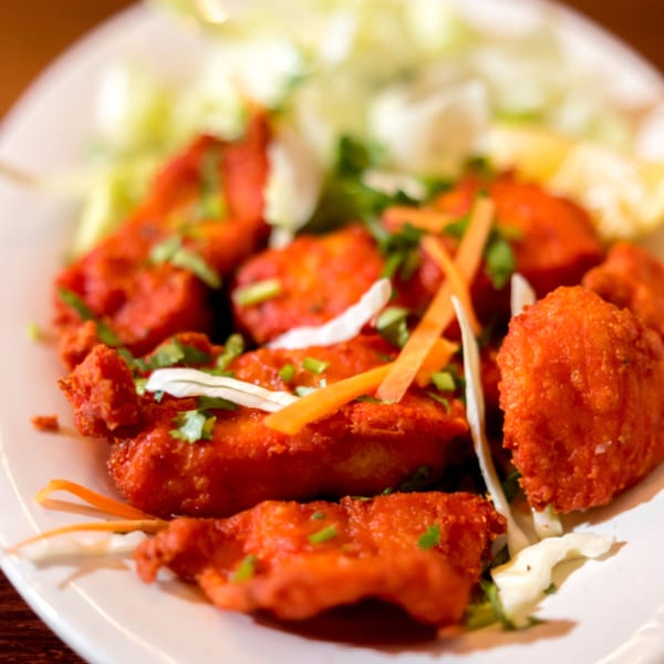 Noorani Kabab House's vibrant red Indian chicken pakora, garnished with fresh herbs and shredded vegetables.