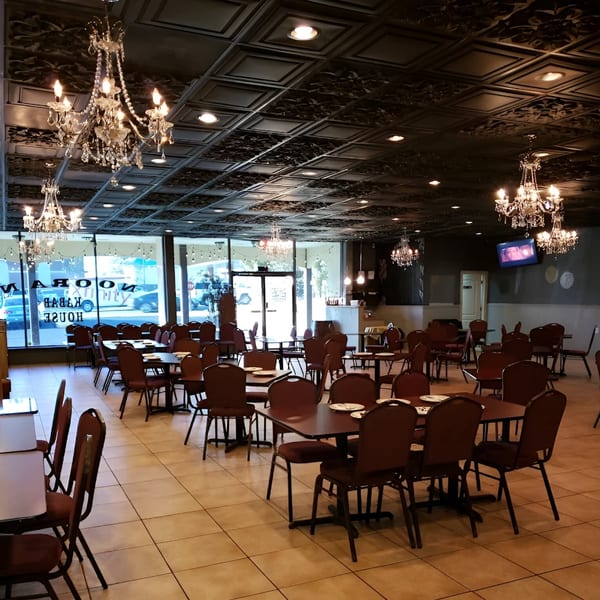 Noorani Kabab House dining room with chandeliers, tables, and chairs, seen from the entrance.