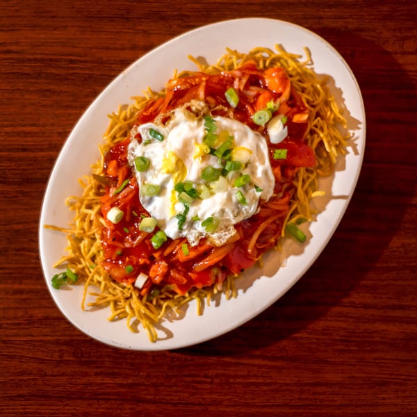 Noorani Kabab House's Indian-style noodles with red sauce, vegetables, a fried egg, and green onions.